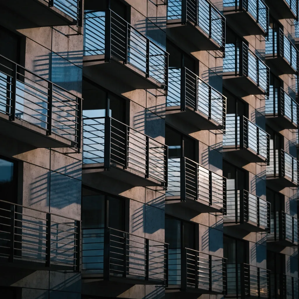 Fachada residencial de viviendas en hilera al anochecer, con ventanales repetidos y luz azulada sobre el cristal
